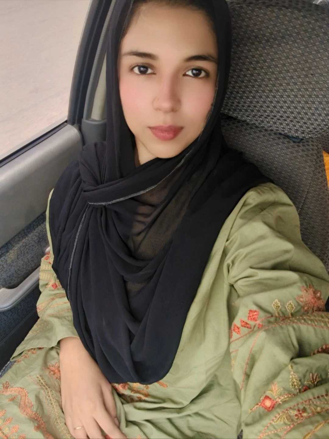 Zarqoon Saeed portrait — green embroidered shalwar kameez and black draped hijab, soft daylight